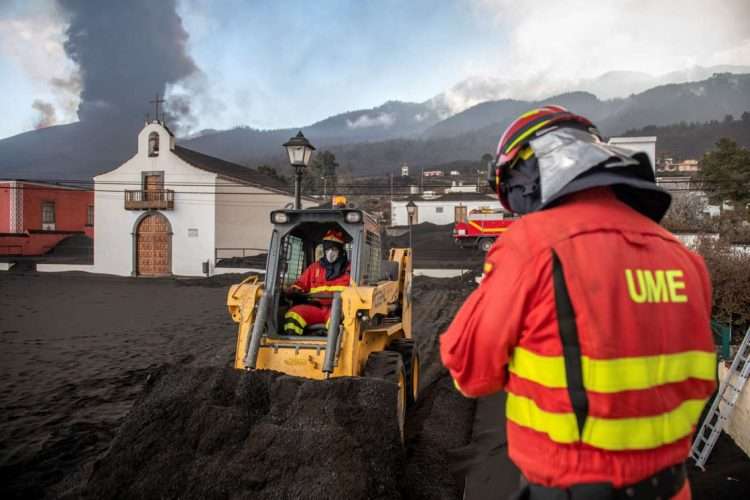 Personal de la Unidad de Emergencia Militar limpia ceniza negra del volcán mientras continúa haciendo erupción de lava detrás de una iglesia en la isla de La Palma. Foto: Saul Santos/AP.
