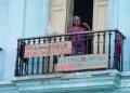 Una mujer se asoma al balcón donde se halla un cartel de apoyo a los familiares de las víctimas de la explosión en el hotel Saratoga, en un edificio cercano al lugar. Foto: Otmaro Rodríguez.