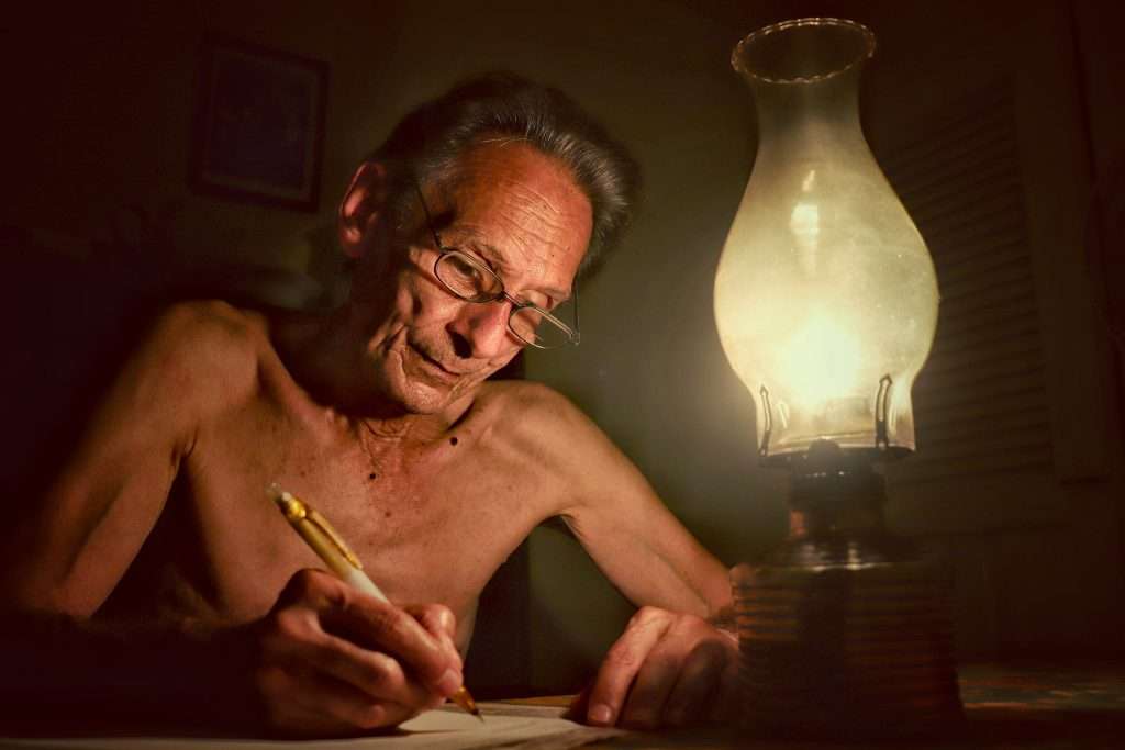 Anciano escribe durante un corte de energía eléctrica en Cuba, apagones, Cienfuegos de la serie Escenas Domésticas 2022 Franko
