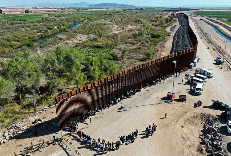Inmigrantes esperan para ser procesados por la Patrulla Fronteriza en la barrera entre EE. UU. y México en Yuma, Arizona. Foto: CBS.