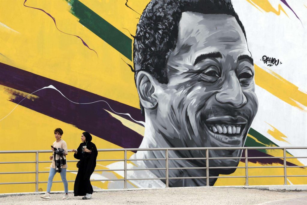 mujeres pasan delante de un mural que representa al exjugador brasileño Edson Arantes do Nascimento, "Pelé" enfrente del estadio Al Khalifa de Doha, Catar, este viernes. EFE/Antonio Lacerda