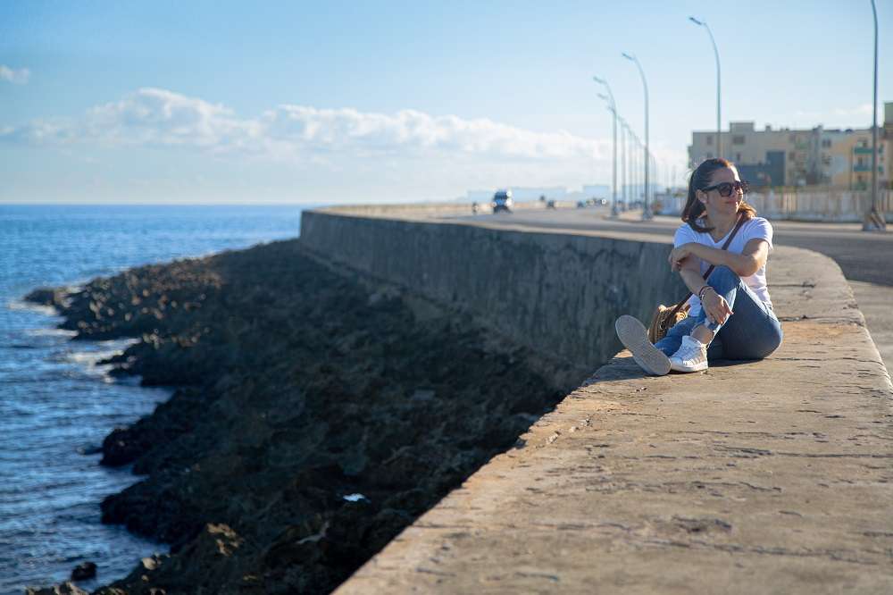 Mujer sentada en el muro del malecón de la habana frente al mar foto jorge ricardo