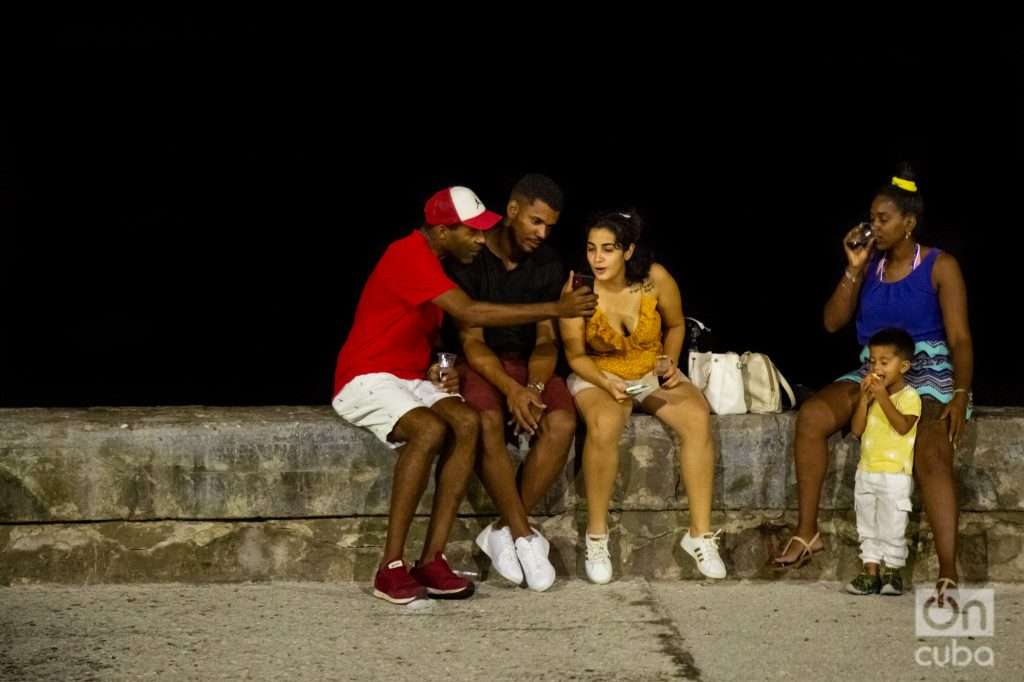 Grupo de personas miera la pantalla de un celular en el muro del Malecón de La Habana. Foto: Jorge Ricardo.