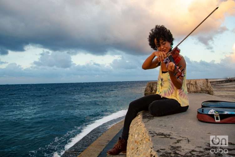 Mujer toca violín sentada en el muro del malecón de La Habana con el mar de fondo Cuba 2022 Foto: Jorge Ricardo