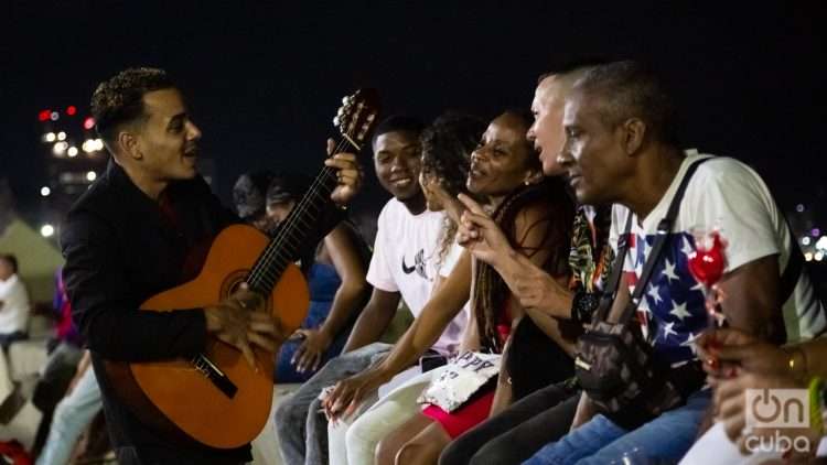 Grupo de personas en el muro del malecón de la Habana escucha a un músico aficionado con su guitarra de noche. Foto: Jorge Ricardo