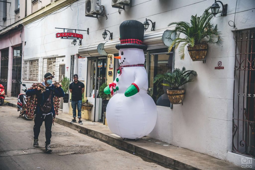 En una calle de Centro Habana un muñeco inflable navideño custodia un restaurante mientras pasa vendedor de cebollas 2021