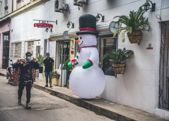 En una calle de Centro Habana un muñeco inflable navideño custodia un restaurante mientras pasa vendedor de cebollas 2021