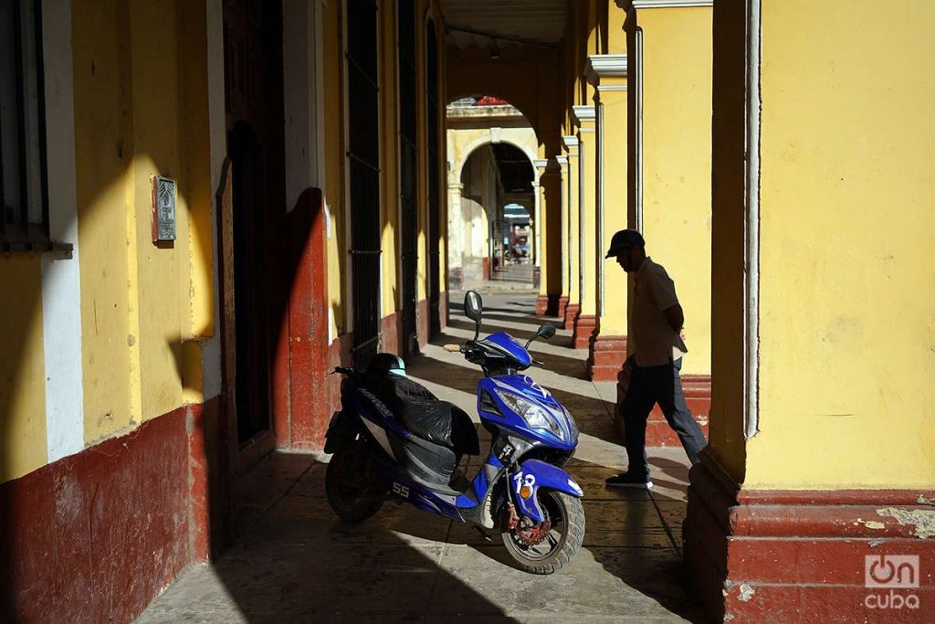 Hombre camina junto a una moto eléctica en un pórtico de La Habana, Cuba, 2023. Foto: Alejandro Ernesto.