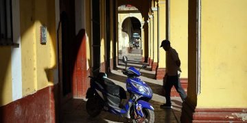 Hombre camina junto a una moto eléctica en un pórtico de La Habana, Cuba, 2023. Foto: Alejandro Ernesto.