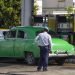 Un policía (de espaldas) observa a un coche antiguo en una gasolinera, en La Habana. Foto: Yander Zamora/EFE