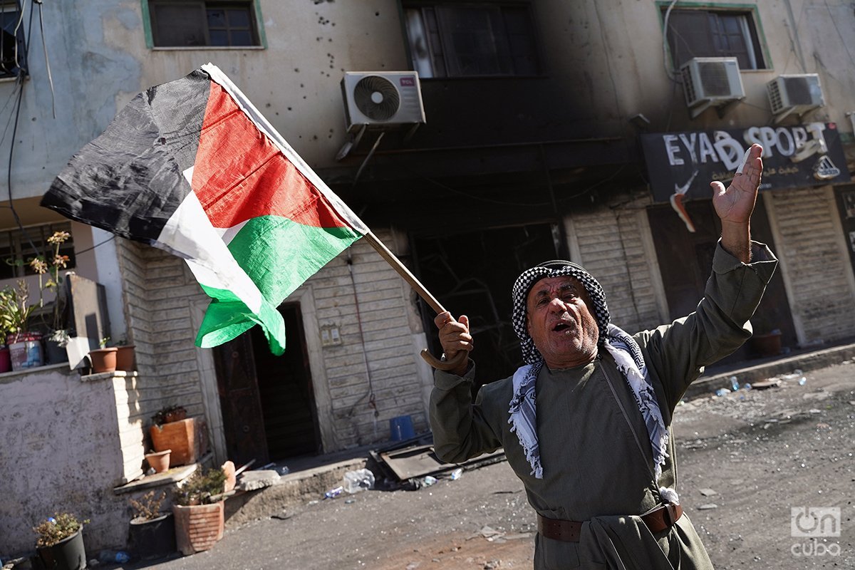 Un anciano con una bandera palestina recorre el campo arengando a la gente.
