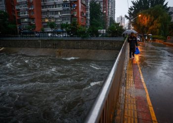 Un hombre camina sobre un puente, en medio de una inundación, en Pekín. Foto: MARK R. CRISTINO/ EFE/EPA.