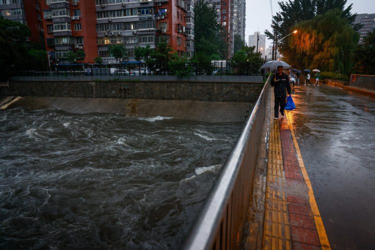 Un hombre camina sobre un puente, en medio de una inundación, en Pekín. Foto: MARK R. CRISTINO/ EFE/EPA.