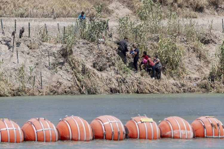 Migrantes al otro lado de la frontera, marcada por la cuestionada barrera flotante. Foto: AFP.
