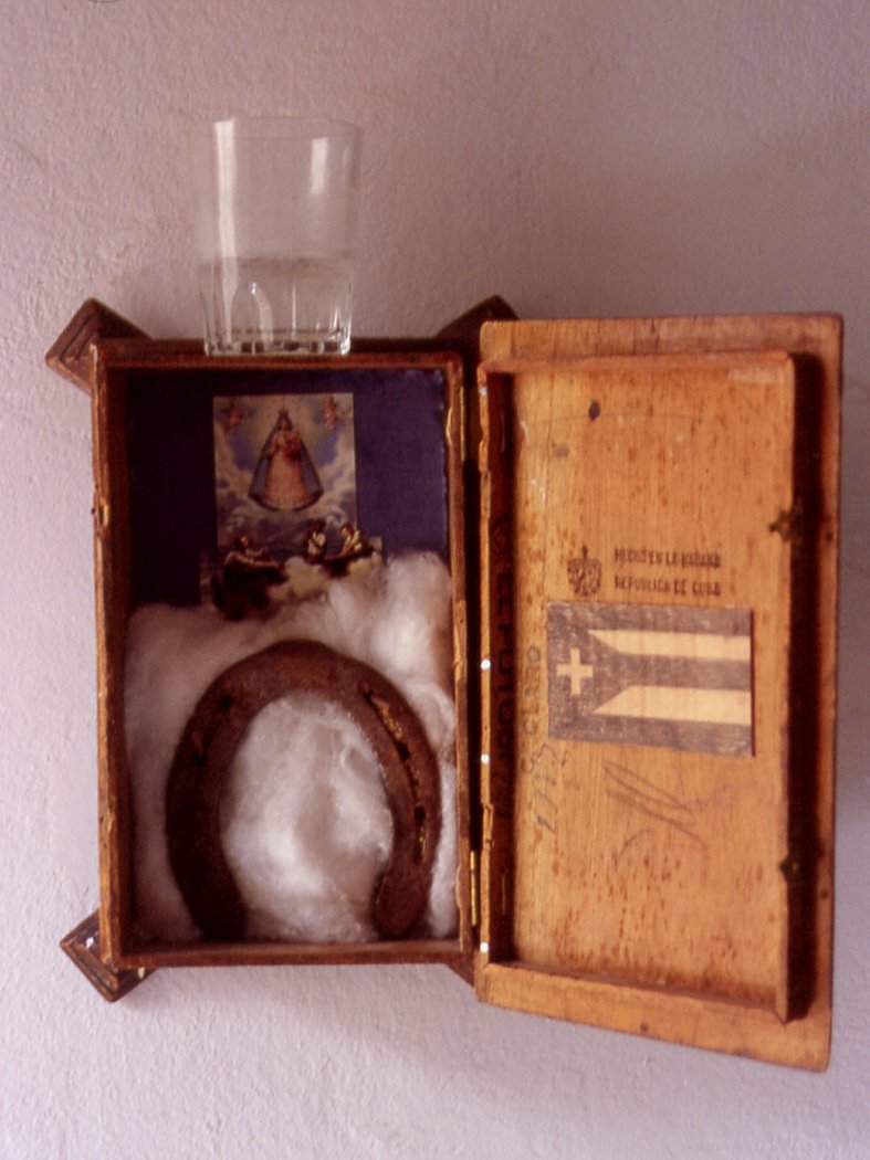 “Por el mar de las Antillas”, 1994. Caja de tabaco, algodón, tela, clavos de hierro, herradura, estampilla, lápiz de color negro, vaso de agua; medidas variables. Barcelona.