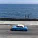 Dos hombres caminan por el muro del malecón de la habana mientras un auto americano recorre la calle, La Habana Cuba, 2023 Foto: Kaloian.