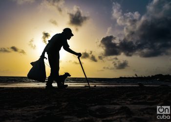 Un anciano con su perro caminan al amanecer por la playa recolectando latas. Foto: Kaloian.