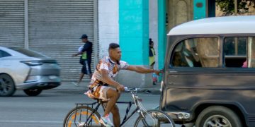 Ciclista se agarra de un auto para no tener que esforzarse en dar pedales, La Habana, Cuba. Foto: Otmaro Rodríguez.