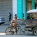 Ciclista se agarra de un auto para no tener que esforzarse en dar pedales, La Habana, Cuba. Foto: Otmaro Rodríguez.