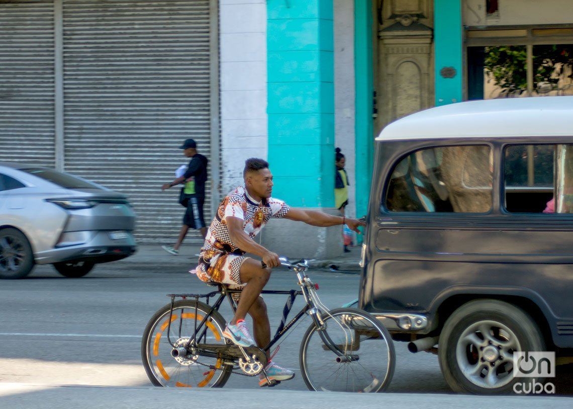 Ciclista se agarra de un auto para no tener que esforzarse en dar pedales, La Habana, Cuba. Foto: Otmaro Rodríguez.