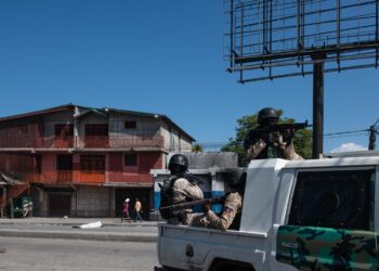 Policías patrullan una calle cercana a la comisaría de Carrefour Aéroport, que fue incendiada por miembros de pandillas en Puerto Príncipe. Foto: Johnson Sabin / EFE.