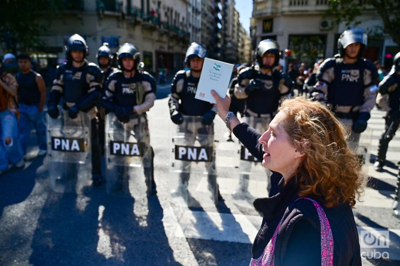 Una manifestante pasa agitando un libro por delante de una fila de las fuerzas de seguridad. Foto: Kaloian.
