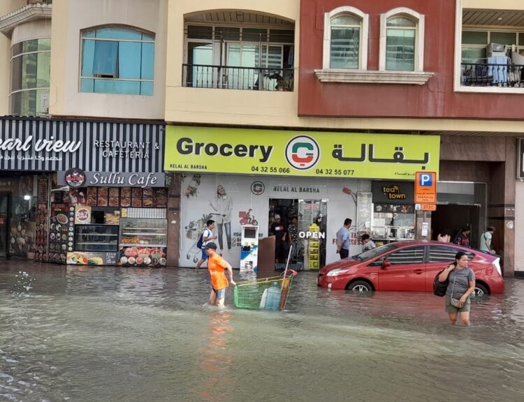 Personas en una calle inundada en el barrio de Al Barsha, días después de las torrenciales lluvias caídas en Dubái. Foto: OnCuba.