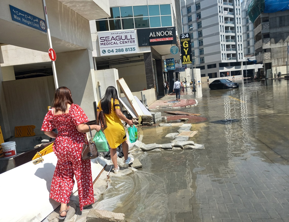 Personas cruzan sobre sacos y bloques puestos en la acera de una calle en Dubái, una semana después de las lluvias que inundaron gran parte de la ciudad. Foto: OnCuba.