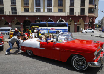 Personas empujan un coche clásico con turistas, en La Habana. Foto: Yander Zamora/EFE.