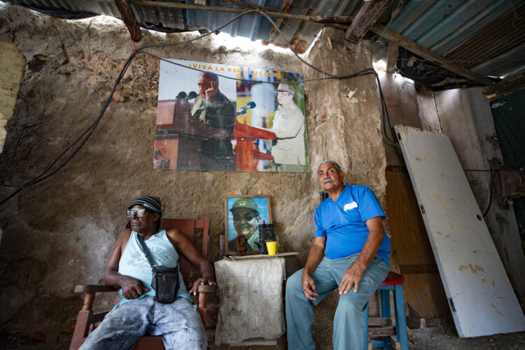 Dos hombres sentados junto a varias imágenes del fallecido líder cubano Fidel Castro y su hermano Raúl Castro al interior de una carpintería en La Habana. Foto: Yander Zamora / EFE.