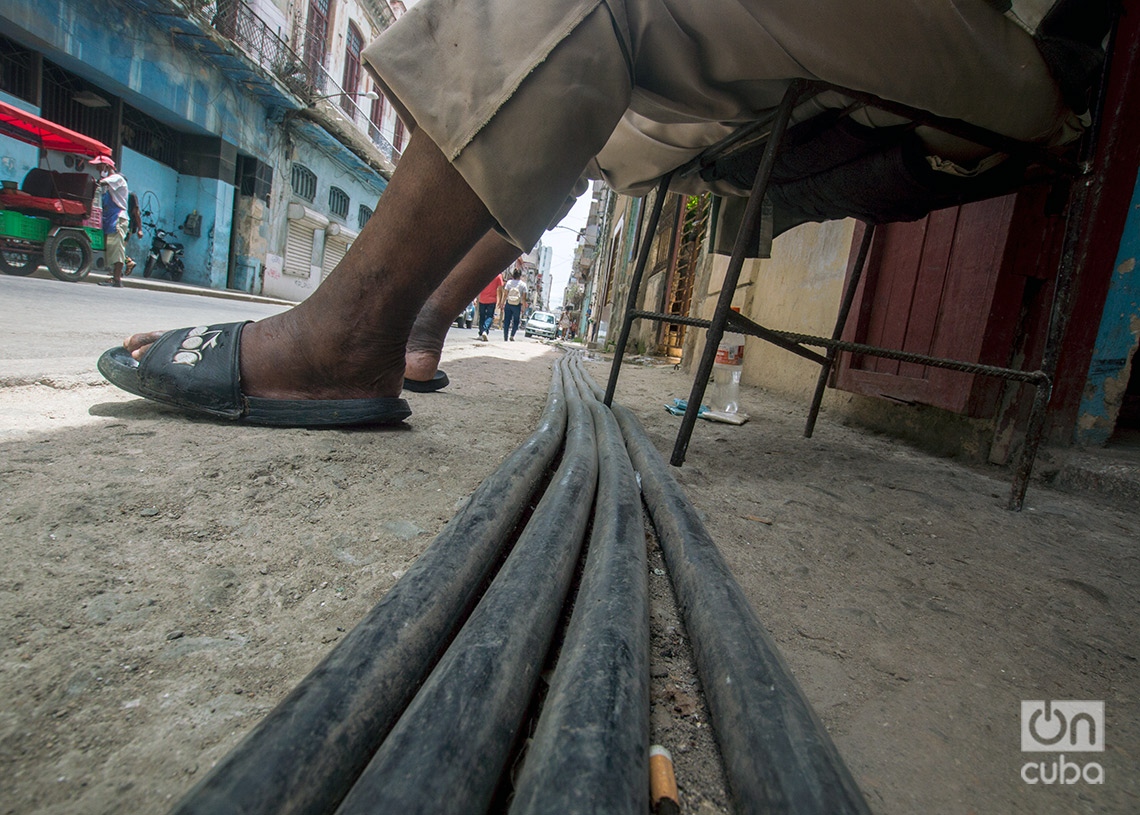 Cables eléctricos al aire libre pasan por debajo de una hombre sentado en una acera rota, en La Habana. Foto: Otmaro Rodríguez.