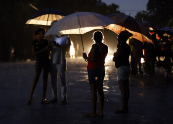 Persona esperan bajo la lluvia la reconexión de la electricidad. Foto: Ernesto Mastrascusa/ EFE.