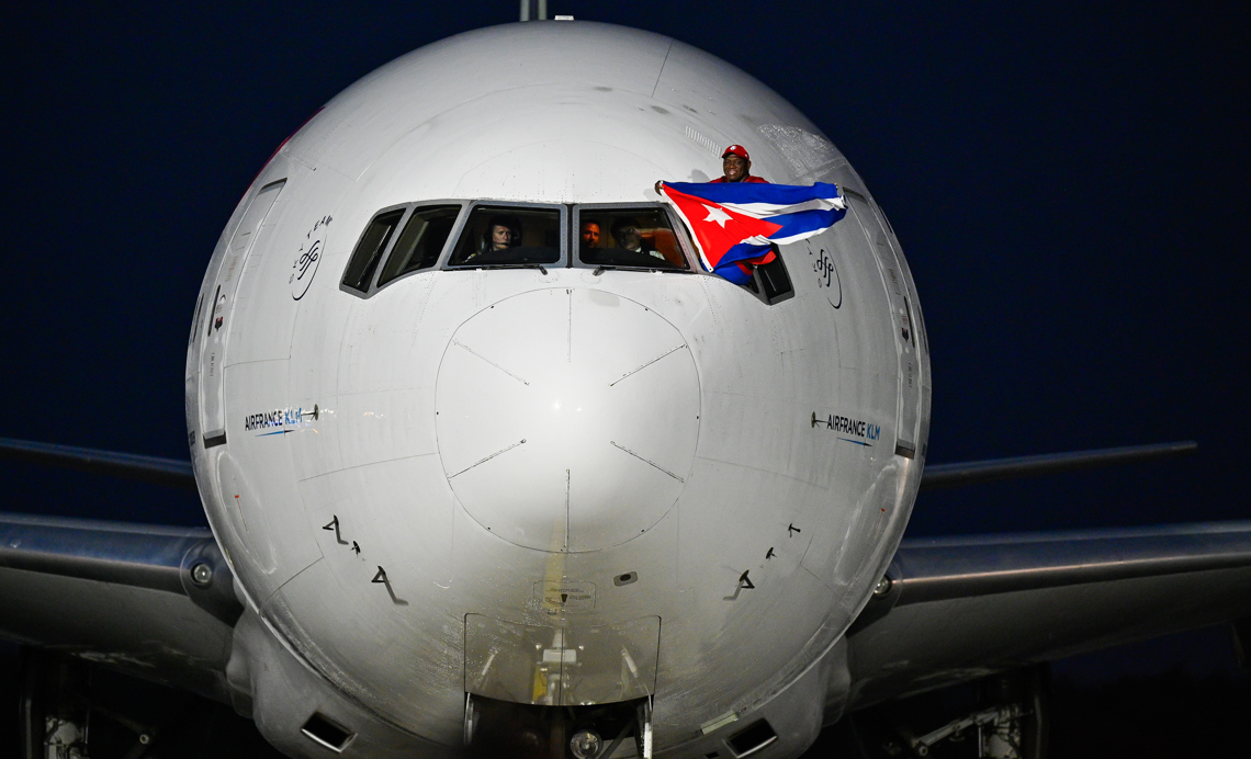 El luchador cubano Mijaín López, cinco veces campeón olímpico, sostiene una bandera de Cuba en la ventanilla del piloto a su llegada este lunes al aeropuerto José Martí de La Habana luego de participar en los Juegos Olímpicos de París 2024. Foto: Adalberto Roque / POOL / AFP vía EFE.