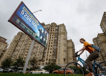 Mujer en bicicleta pasa cerca de un cartel sobre el servicio militar, en Moscú. Foto: YURI KOCHETKOV/EFE/EPA.