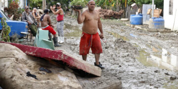 Un hombre camina junto a colchones destruidos en el exterior de una vivienda en la región de San Antonio del Sur una semana después del paso de la tormenta tropical Oscar. Foto: Ernesto Mastrascusa / POOL / EFE.