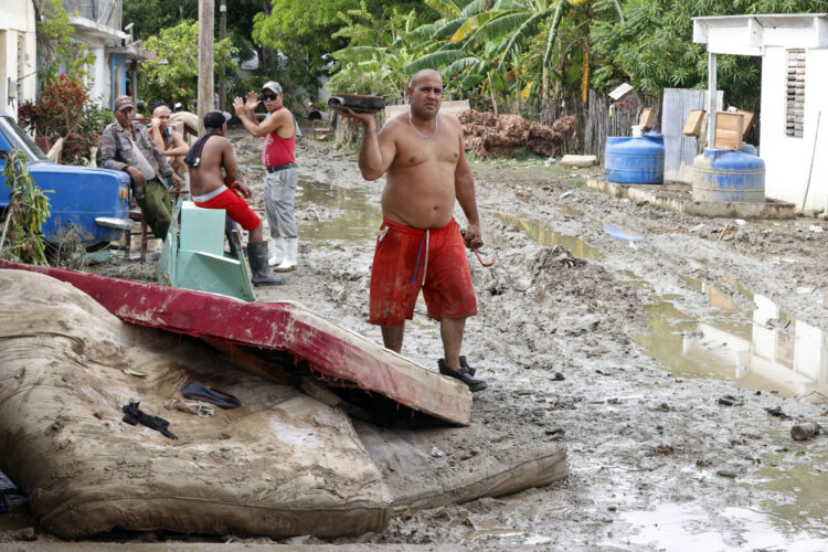 Un hombre camina junto a colchones destruidos en el exterior de una vivienda en la región de San Antonio del Sur una semana después del paso de la tormenta tropical Oscar. Foto: Ernesto Mastrascusa / POOL / EFE.