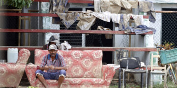 Un hombre descansa en el exterior de una vivienda en la región de San Antonio del Sur una semana después del paso de la tormenta tropical Oscar. Foto: Ernesto Mastrascusa / POOL / EFE.