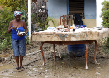 Una mujer sostiene un teléfono en el exterior de una vivienda en la región de San Antonio del Sur una semana después del paso de la tormenta tropical Oscar. Foto: Ernesto Mastrascusa / POOL / EFE.