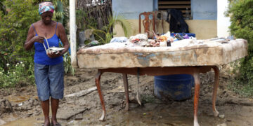 Una mujer sostiene un teléfono en el exterior de una vivienda en la región de San Antonio del Sur una semana después del paso de la tormenta tropical Oscar. Foto: Ernesto Mastrascusa / POOL / EFE.