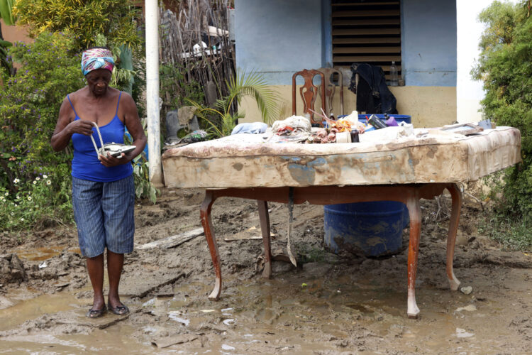 Una mujer sostiene un teléfono en el exterior de una vivienda en la región de San Antonio del Sur una semana después del paso de la tormenta tropical Oscar. Foto: Ernesto Mastrascusa / POOL / EFE.