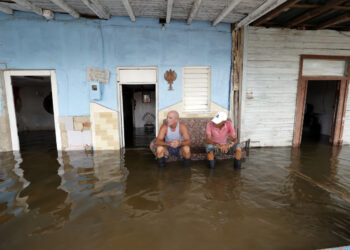 Personas descansan frente a casas afectadas por las inundaciones provocadas por el huracán Milton en Batabanó, en la costa sur del occidente de Cuba. Foto: Ernesto Mastrascusa / EFE.