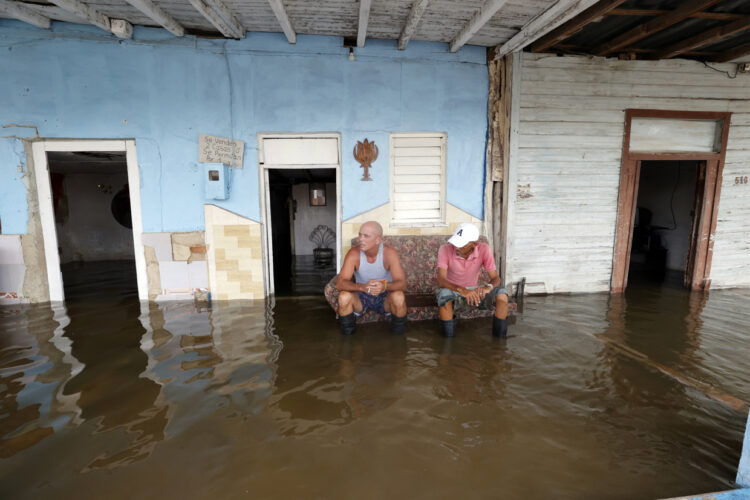 Personas descansan frente a casas afectadas por las inundaciones provocadas por el huracán Milton en Batabanó, en la costa sur del occidente de Cuba. Foto: Ernesto Mastrascusa / EFE.