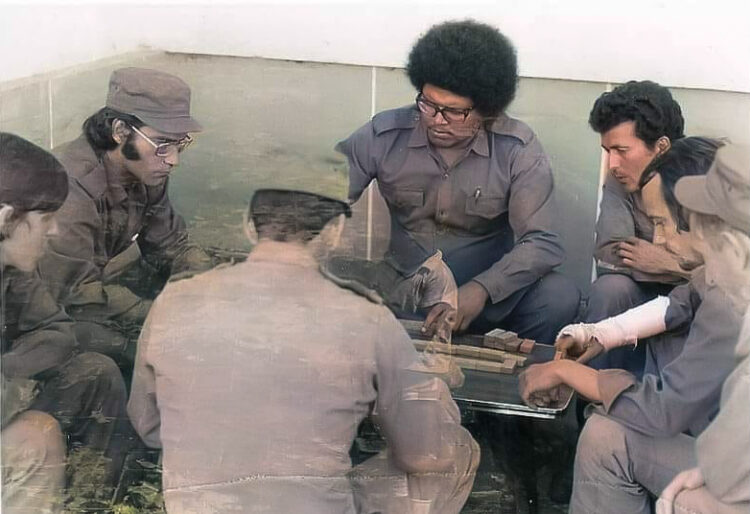 Noel Nicola (delante, de perfil), Vicente Feliú, Pablo Milanés y Silvio Rodríguez, junto a otros presentes, en torno a una mesa de dominó en Luanda, Angola, 1976.