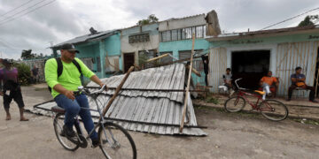 Un hombre transita en bicicleta frente a una vivienda con el techo caído tras el paso del huracán Rafael, en la provincia de Artemisa. Foto: Ernesto Mastrascusa / EFE.