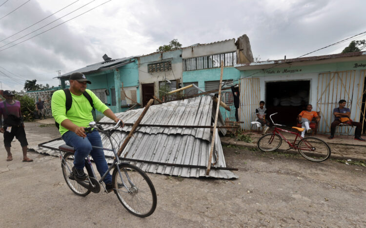 Un hombre transita en bicicleta frente a una vivienda con el techo caído tras el paso del huracán Rafael, en la provincia de Artemisa. Foto: Ernesto Mastrascusa / EFE.