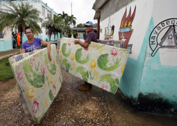 Dos personas cargan unos colchones ante la llegada del huracán Rafael, en Surgidero de Batabanó. Foto:  Ernesto Mastrascusa/EFE.