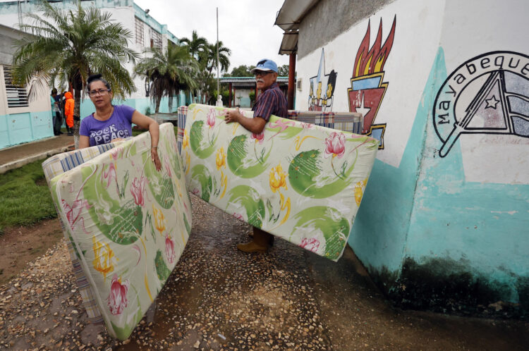 Dos personas cargan unos colchones ante la llegada del huracán Rafael, en Surgidero de Batabanó. Foto:  Ernesto Mastrascusa/EFE.