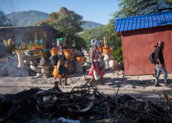 Personas pasan frente a los restos de una hoguera donde incineraron a un pandillero, en una calle de Puerto Príncipe. Foto: Johnson Sabin/EFE.