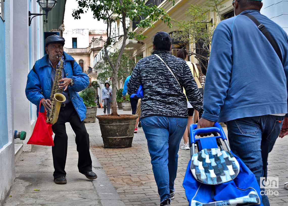 Un hombre toca música mientras otras personas se dirigen hacer compras, en el centro histórico de La Habana, en los primeros días de 2025. Foto: Otmaro Rodríguez.