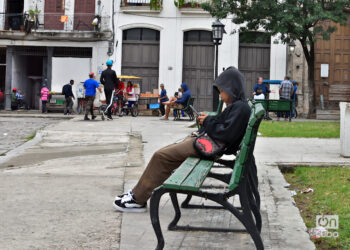 Un estudiante abrigado revisa su teléfono móvil en un parque de La Habana, tras la llegada de un frente frío a Cuba. Foto: Otmaro Rodríguez.